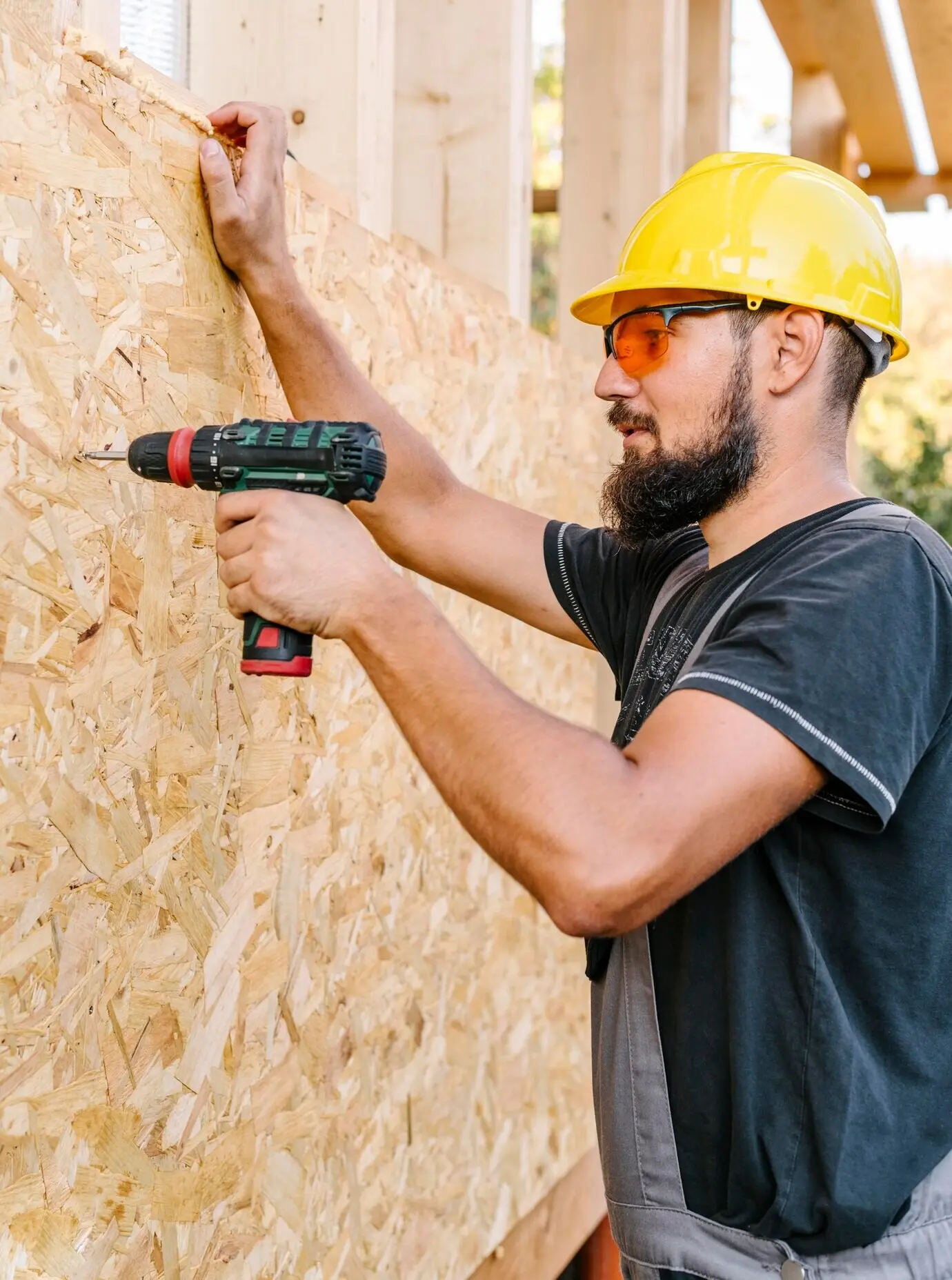 Profile view of a construction worker drilling into plywood.