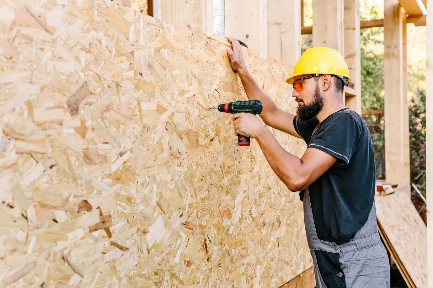 Profile view of a construction worker drilling into plywood, with copy space.